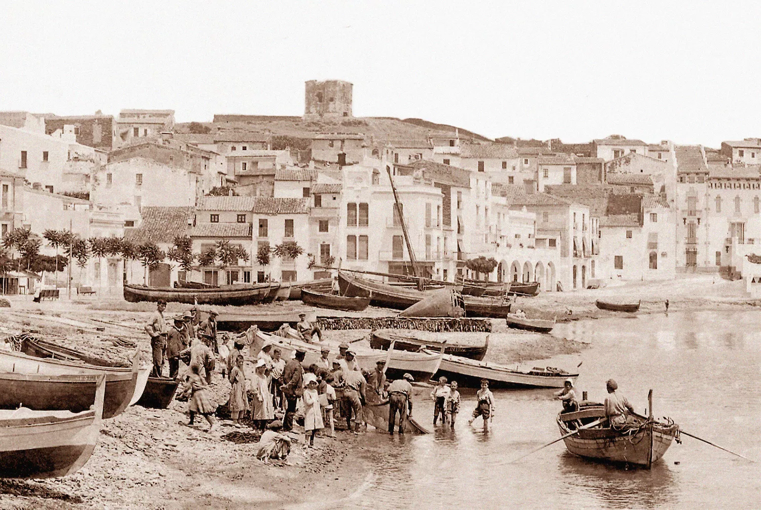 La façana marítima de Cadaqués amb les barques a la platja, l’any 1917. Al fons, dalt del turó, la torre de les Creus ja en una condició ruïnosa