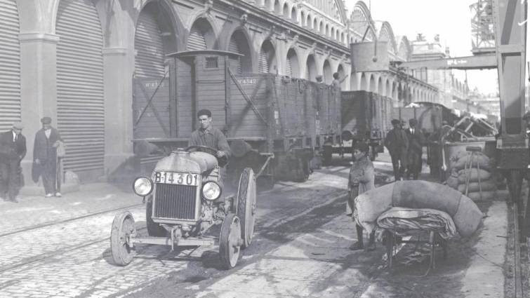 Magatzems del moll de Bosch i Alsina del port de Barcelona, amb tres vagons de càrrega que avancen per les vies del ferrocarril