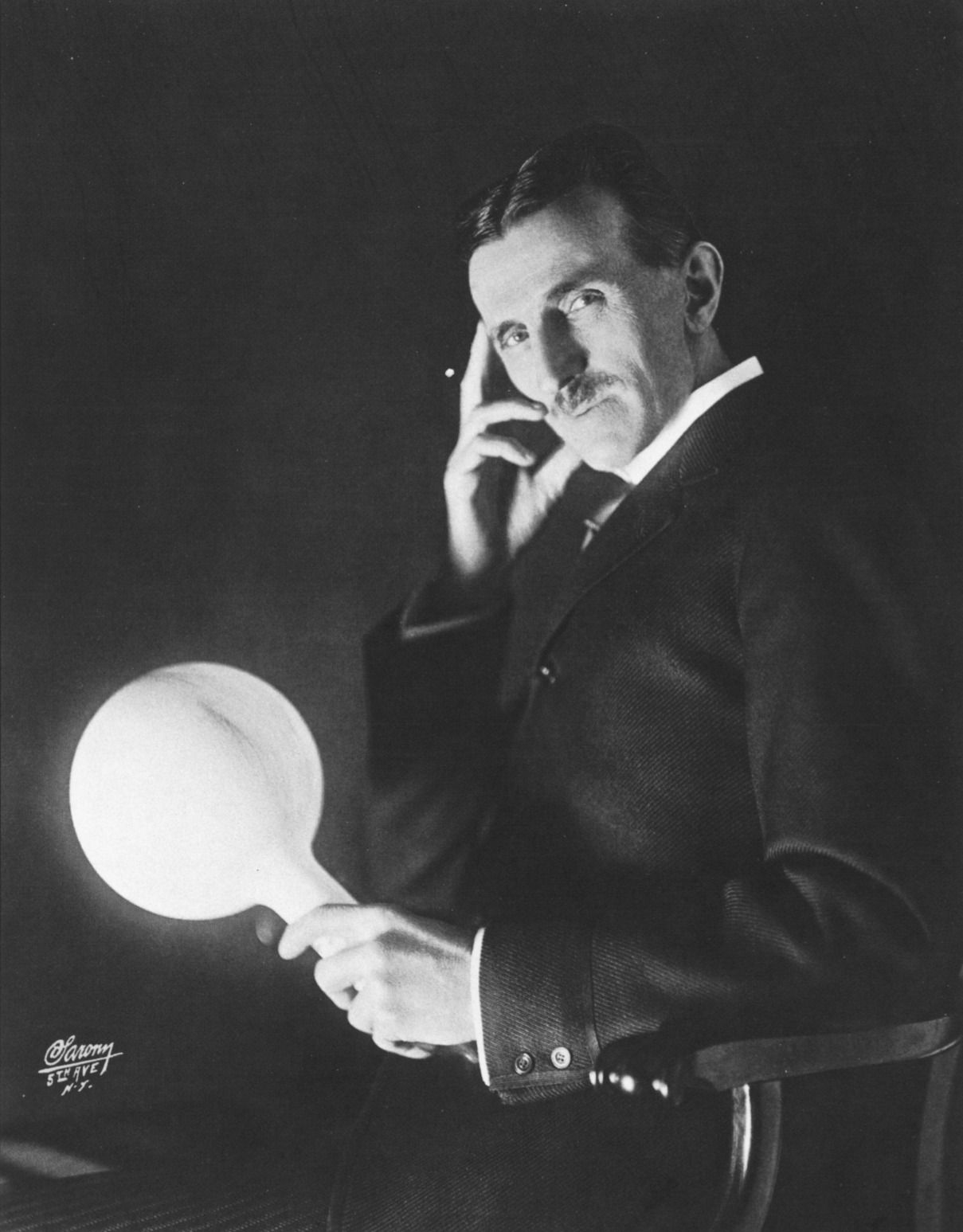Nikola Tesla sostenint una làmpada en un dels seus experiments