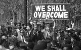 Martin Luther King i, al darrere, dues persones que sostenen una pancarta amb la frase 'We shall overcome'