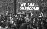 Martin Luther King i, al darrere, dues persones que sostenen una pancarta amb la frase 'We shall overcome' Martin Luther King i, al darrere, dues persones que sostenen una pancarta amb la frase 'We shall overcome'